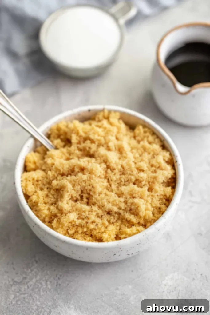 A homemade brown sugar substitute in a white bowl with a spoon sticking out. A small jug of molasses rests nearby. 