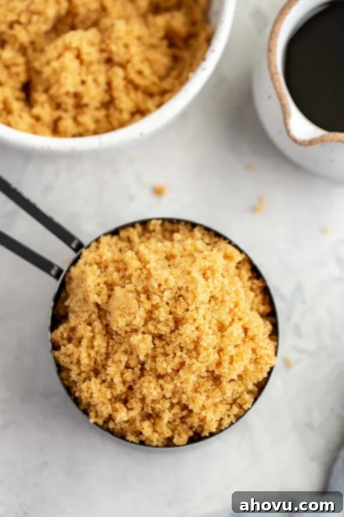An overhead view of a measuring cup of homemade brown sugar. A bowl of brown sugar and a small jug of molasses rest nearby. 