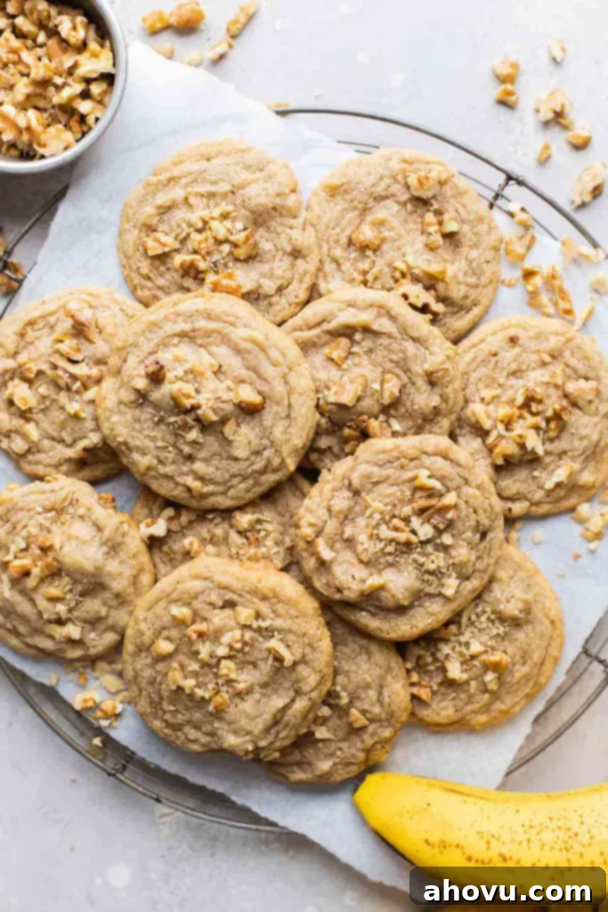 An overhead view of a delicious pile of banana nut cookies cooling on a wire rack, with scattered chopped walnuts and a ripe banana on the side, showcasing their perfect golden-brown exterior.