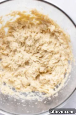 An overhead view of a glass mixing bowl filled with the combined wet ingredients – mashed banana, egg yolk, and vanilla extract – for the banana cookies.