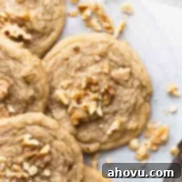 Several banana cookies on a wire rack with a piece of parchment paper underneath them. Pieces of chopped walnuts are scatter on top of and around the cookies.