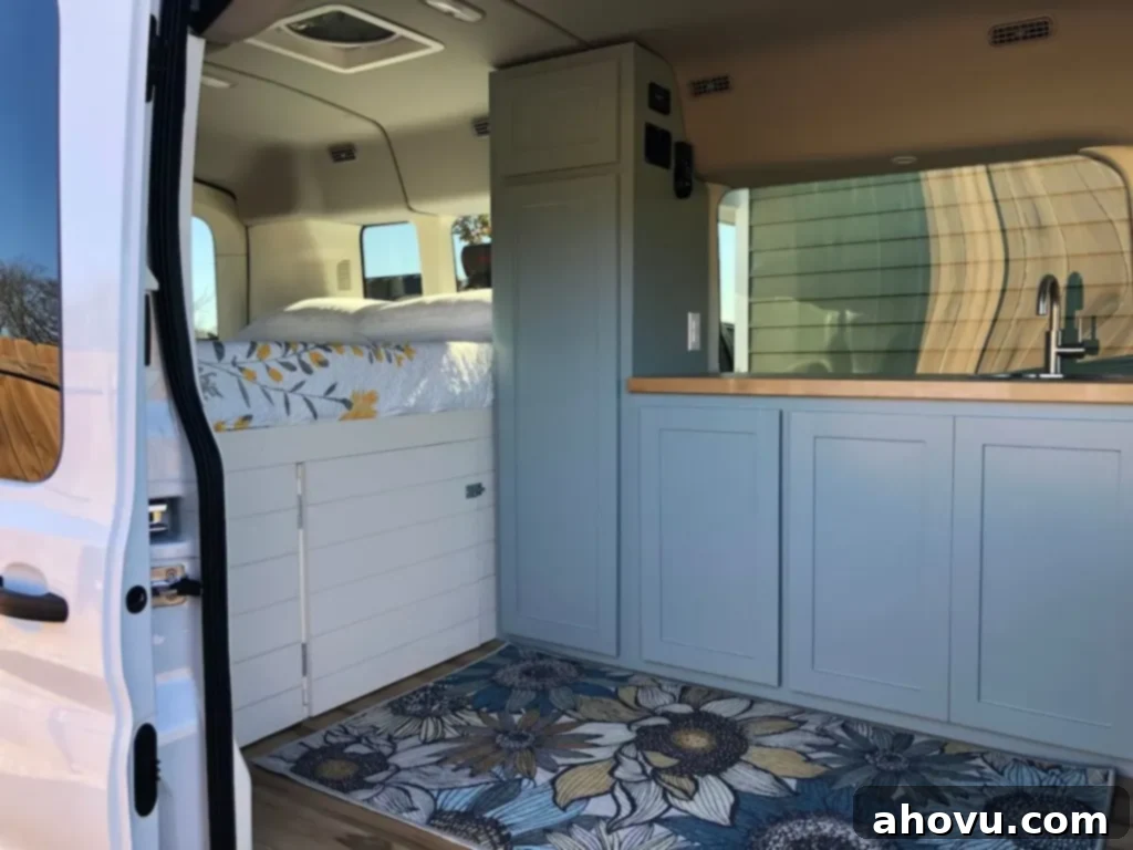 Kitchen Chronicles and Personal News 4 A beautifully renovated cargo van interior featuring a cozy bed with ample storage underneath, elegant blue cabinets, a functional sink, and a vibrant blue rug adorned with floral patterns, ready for adventure.