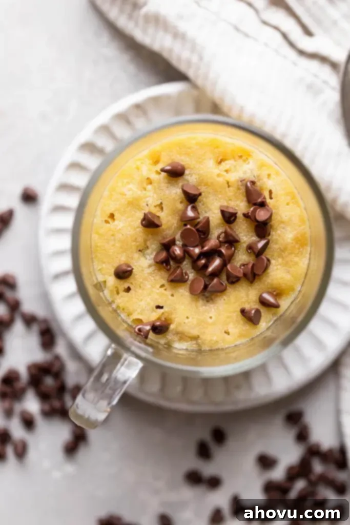 Decadent Chocolate Chip Mug Fix 5 A close-up, overhead view of a perfectly baked chocolate chip cookie in a mug, garnished with extra mini chocolate chips on top. The cookie's golden-brown edges and soft, melted chocolate center are visible, making it an inviting single-serve dessert.