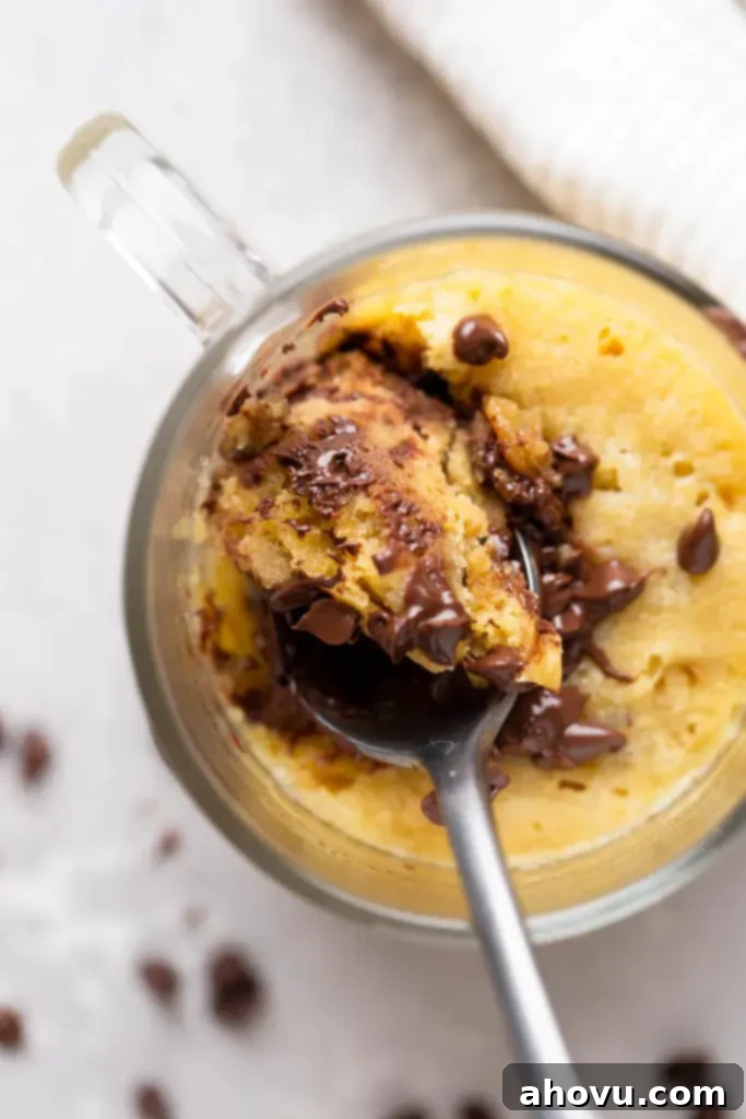 Decadent Chocolate Chip Mug Fix 6 An overhead shot captures a spoon digging into the warm, soft center of a microwave chocolate chip mug cookie, revealing its gooey texture and melted chocolate chips. This image perfectly illustrates the indulgent experience of eating this quick dessert.