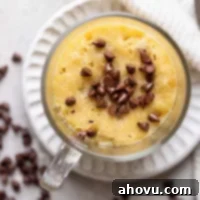 Decadent Chocolate Chip Mug Fix 7 An overhead view of a warm, perfectly baked chocolate chip cookie in a mug, its top studded with melted mini chocolate chips and golden-brown edges.