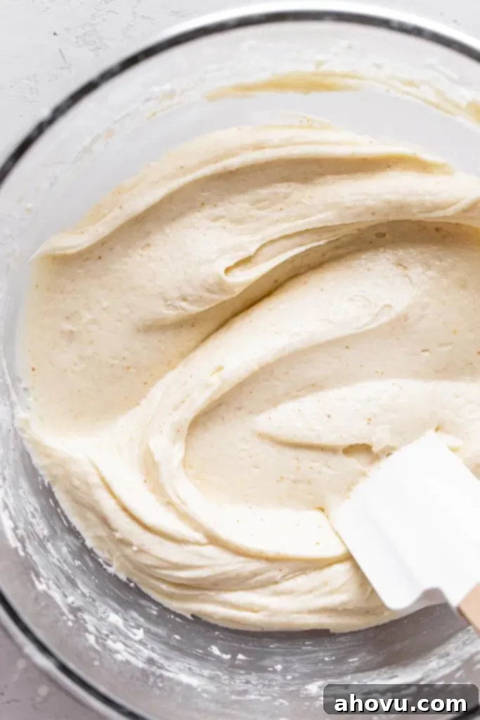 An overhead view of a glass mixing bowl full of brown butter cream cheese frosting. A rubber spatula rests in the bowl. 