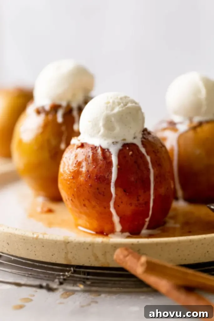 Three stuffed baked apples topped with vanilla ice cream on a speckled white plate. 