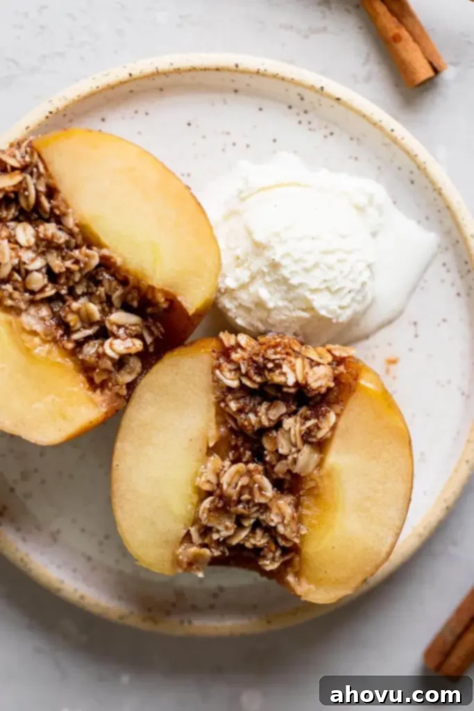 An overhead view of a baked apple that's been cut in half to show the oat filling. A scoop of ice cream is also on the speckled plate. 