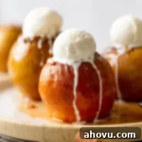 Three baked apples topped with ice cream on a white speckled plate.