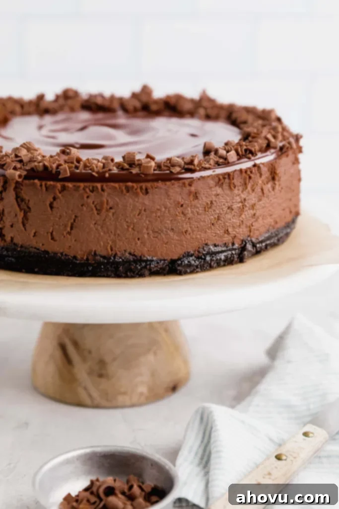 A side view of a chocolate cheesecake on a white marble cake stand. A small bowl of chocolate shavings rests in the foreground. 