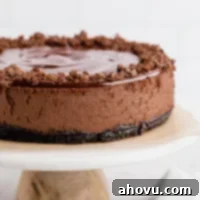 A chocolate cheesecake sitting on top of a marble cake stand. The cheesecake is topped with chocolate ganache and garnished with chocolate curls.