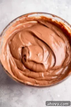 An overhead view of a smooth chocolate cheesecake filling in a glass mixing bowl.
