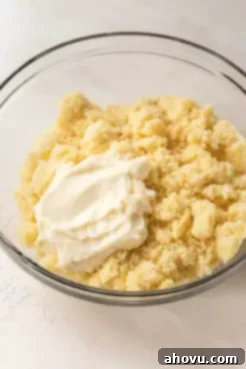 Crumbled vanilla cake in a glass bowl with a dollop of buttercream frosting on top.