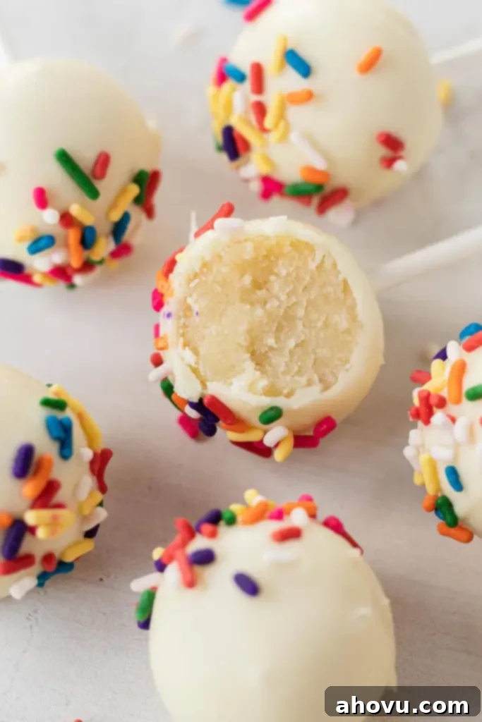 A close up view of vanilla cake pops topped with sprinkles. One cake pop has a bite missing. 