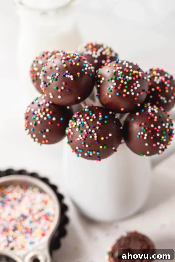 A beautiful bouquet of homemade chocolate cake pops, elegantly arranged in a white vase, with colorful sprinkles scattered in the foreground, ready for a celebration.