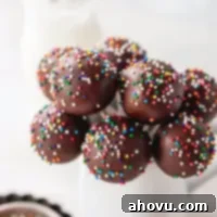 Several chocolate cake pops topped with sprinkles in a small white jar.
