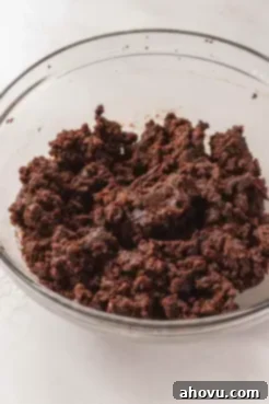 Another view of a glass mixing bowl, this time showing crumbled chocolate cake and a dollop of chocolate buttercream, well-combined and ready for shaping.
