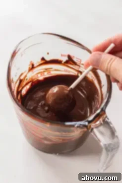 A chocolate cake pop being carefully dunked into a glass of smooth, melted chocolate, showing the precise moment of coating.