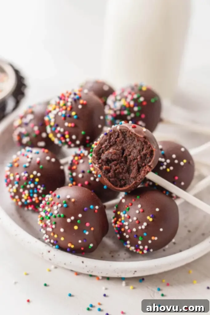 A close-up shot of several perfectly crafted chocolate cake pops, arranged on a white speckled plate, with one cake pop showing a delicious bite missing, highlighting its appealing texture.