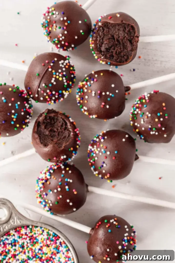 An inviting overhead photograph of an array of finished chocolate cake pops, artfully dipped in chocolate and adorned with colorful sprinkles, with two of them showing a delightful bite taken out, inviting viewers to taste.