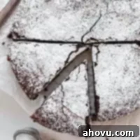 An overhead view of a flourless chocolate cake topped with powdered sugar. Two slices have been cut from the cake and one is being removed.