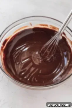 A glass mixing bowl full of melted chocolate. A whisk rests on the side.
