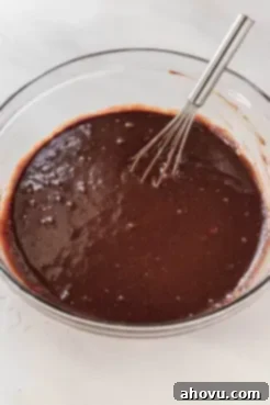 A glass mixing bowl full of cake batter. A whisk rests on the side.