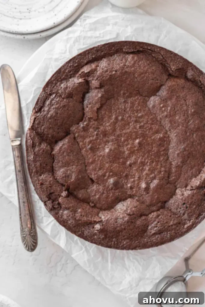An overhead view of a flourless chocolate cake on a square of parchment paper. A butter knife rests on the side. 
