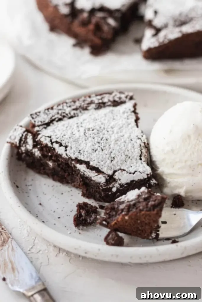 A slice of flourless cake dusted with powdered sugar on a white plate with a scoop of ice cream. 