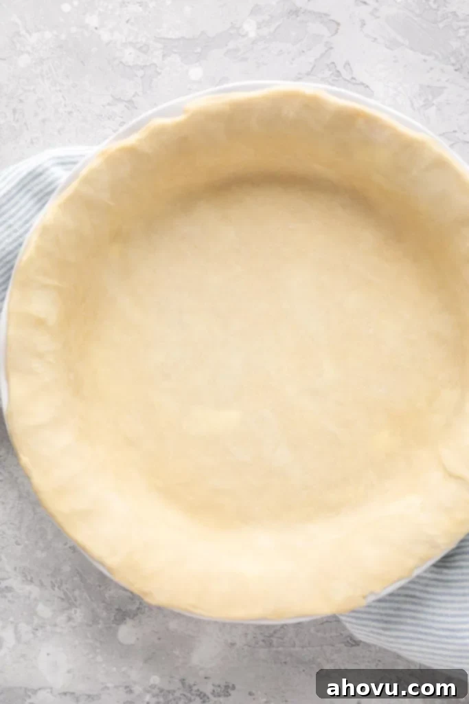 An unbaked pie crust inside of a white pie dish. The dish is placed on top of a blue and white striped napkin.