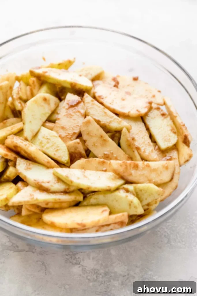 Apple slices coated in a mixture of flour, spices, and lemon juice in a glass bowl.