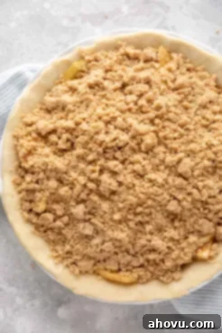 An unbaked apple crumble pie that's been topped with the crumb topping and is ready to go into the oven.