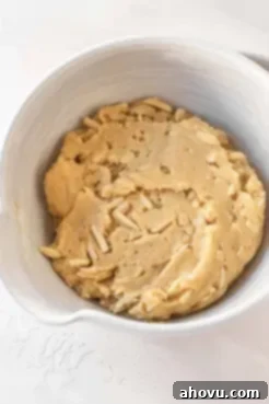 An overhead view of a white mixing bowl full of almond biscotti dough.
