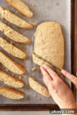 An overhead view of a log of once-baked biscotti being sliced into cookies.