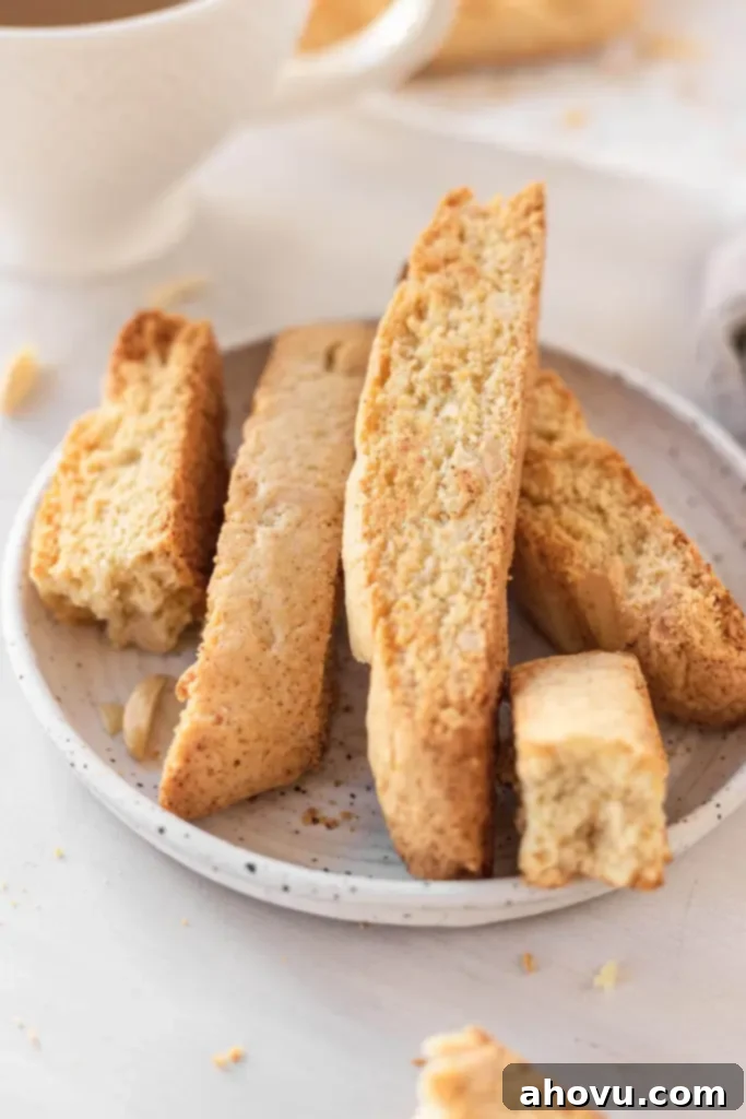 Homemade Almond Biscotti Perfection 4 Almond biscotti on a white speckled plate. One cookie has been broken into pieces.