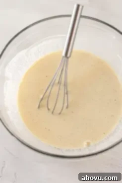 Buttermilk, sour cream, eggs, and vanilla mixed together in a glass mixing bowl with a metal whisk.