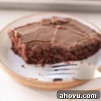 A slice of Texas sheet cake on a white speckled plate. A bite has been taken out of the slice and a fork rests on the side of the plate.
