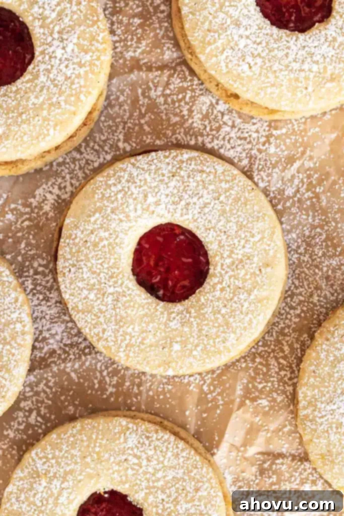 Peekaboo Jam Cookies 2 A close-up, overhead view of beautifully dusted Linzer cookies with raspberry jam centers, arranged on parchment paper, ready to be enjoyed.