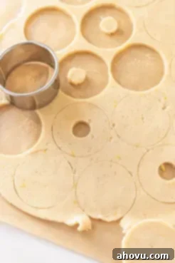Rolled out Linzer cookie dough on parchment paper with a round cookie cutter in action, preparing the cookie shapes.