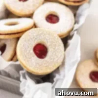 Peekaboo Jam Cookies 7 Several Linzer cookies with jam centers and powdered sugar tops are neatly arranged in a loaf pan lined with parchment paper.