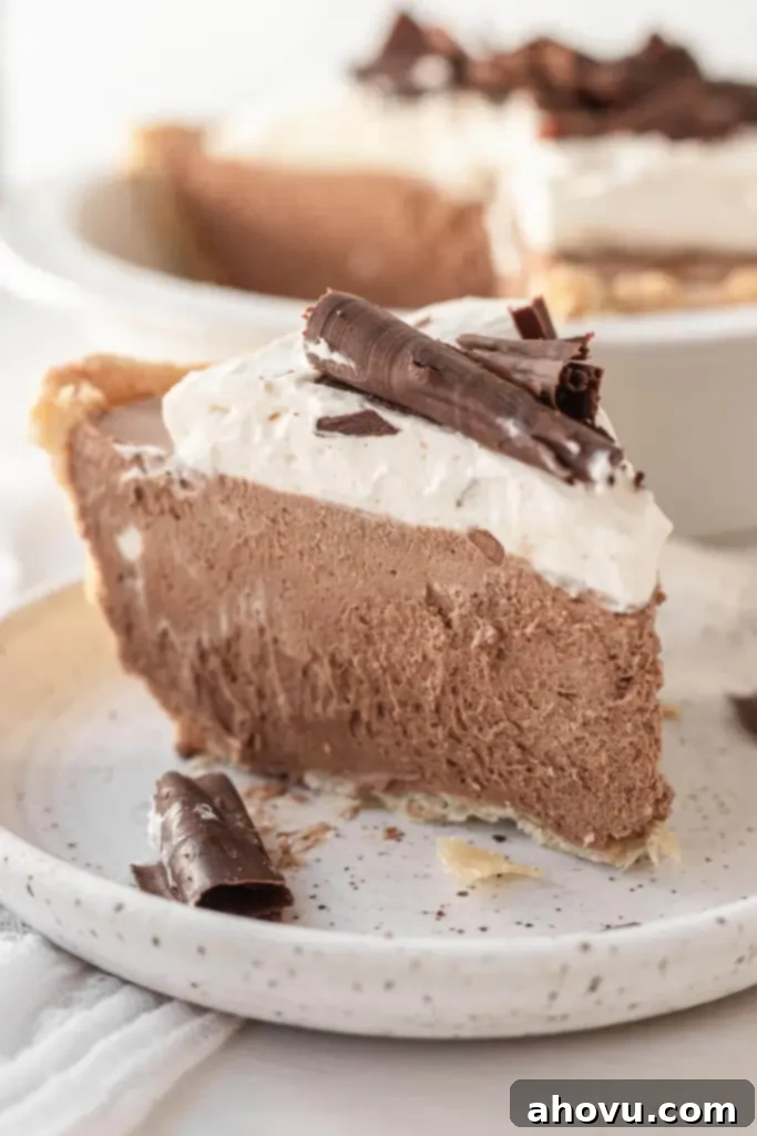 Decadent French Silk Pie 4 A side view of a slice of French silk chocolate pie on a speckled white plate. The rest of the pie is in a pie plate in the background.