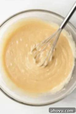 An overhead view of melted butter, sugars, and eggs mixed together in a glass mixing bowl.