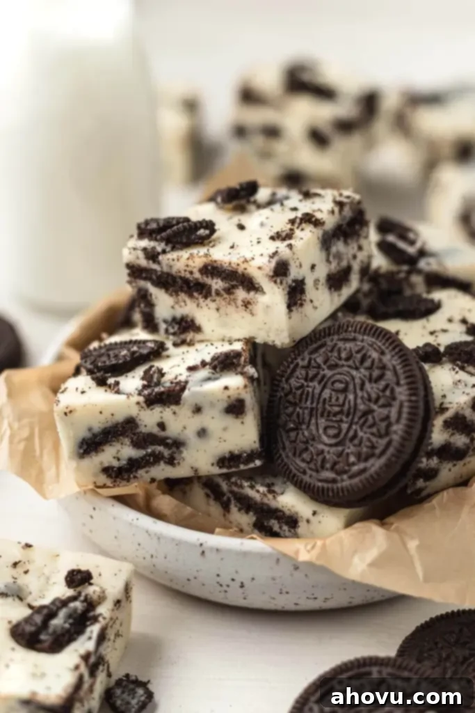 Oreo Cookies and Cream Fudge 41 Slices of rich, creamy Oreo fudge in a white speckled bowl. A vintage glass milk jug sits artfully blurred in the background, suggesting the perfect pairing for this delightful dessert. The fudge is generously studded with crushed Oreo pieces.
