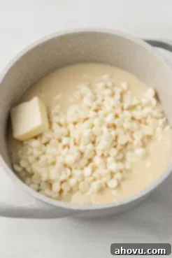 An overhead close-up view of white chocolate chips, butter, and sweetened condensed milk starting to melt together in a saucepan, illustrating the initial step of combining key ingredients for the fudge.