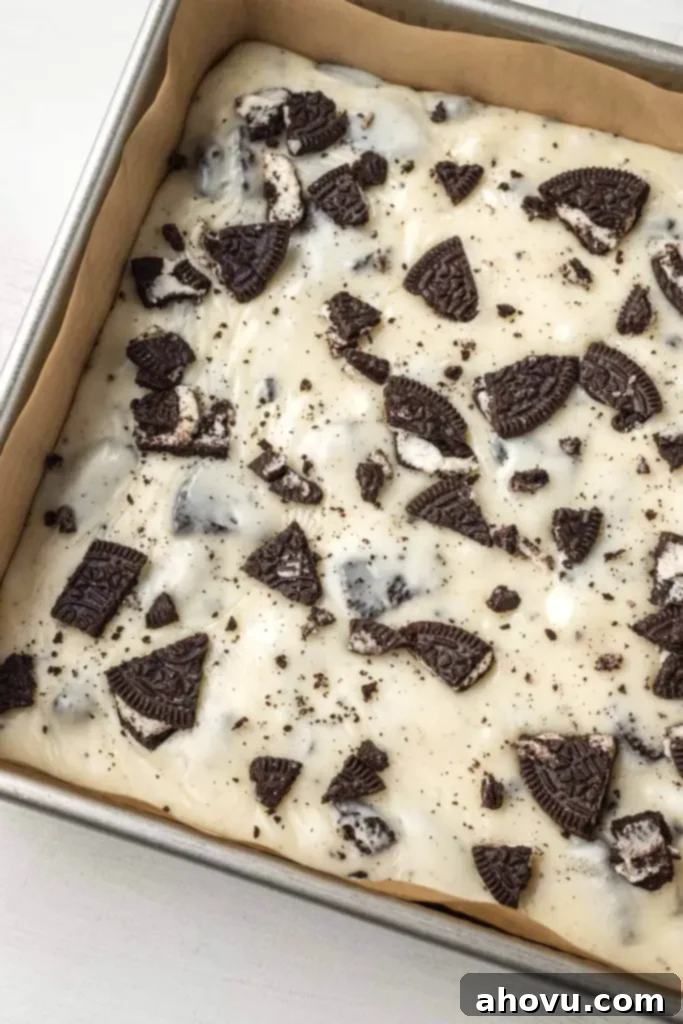 Oreo Cookies and Cream Fudge 4 An inviting overhead view of a full pan of pristine white chocolate Oreo fudge, freshly prepared and ready for chilling. The top is generously scattered with extra crushed Oreo pieces for texture and visual appeal.