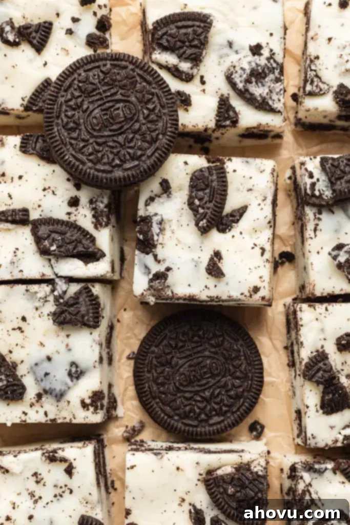 Oreo Cookies and Cream Fudge 5 An overhead shot featuring perfectly sliced pieces of cookies and cream fudge arranged artfully on parchment paper. Two whole Oreo cookies are placed on top of some fudge pieces, enhancing the visual appeal and emphasizing the star ingredient.