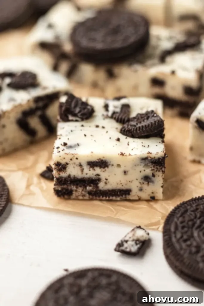 Oreo Cookies and Cream Fudge 6 Several slices of rich, no-bake fudge, visibly studded with crushed Oreos, arranged enticingly on parchment paper. The texture appears smooth and creamy, inviting a taste.