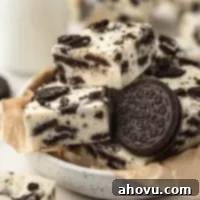 Oreo Cookies and Cream Fudge 8 Several pieces of creamy, delicious Oreo fudge displayed in a bowl lined with brown parchment paper. More pieces of fudge are scattered around the bowl, alongside a charming jug of milk, suggesting a delightful treat.