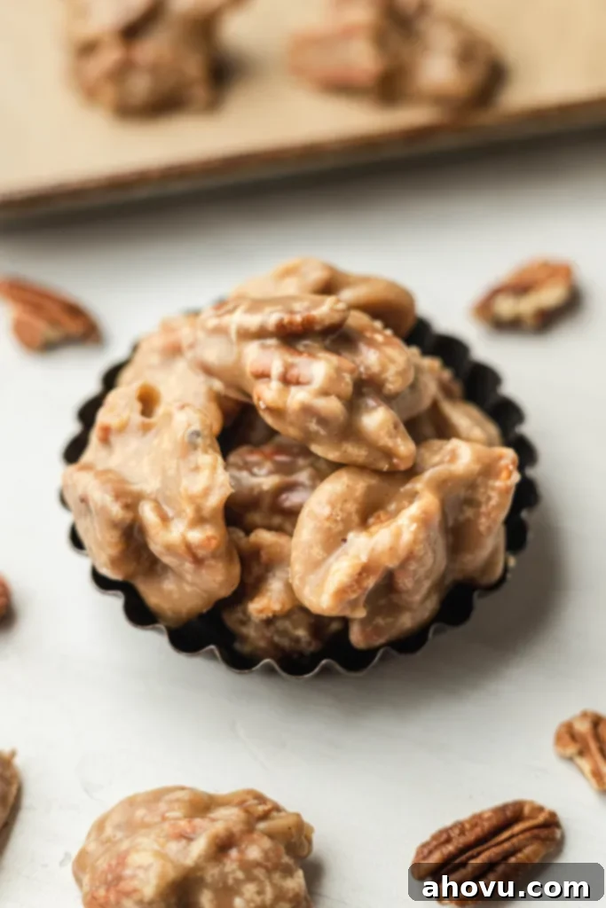 Several southern pecan pralines in a mini tart pan. Pecan halves are scattered around it. 