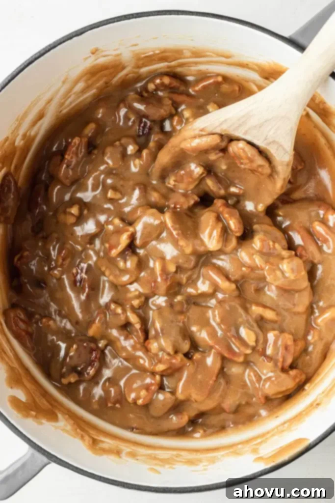 An overhead view of a pot of pecan praline mixture. A wooden spoon rests in the pot. 
